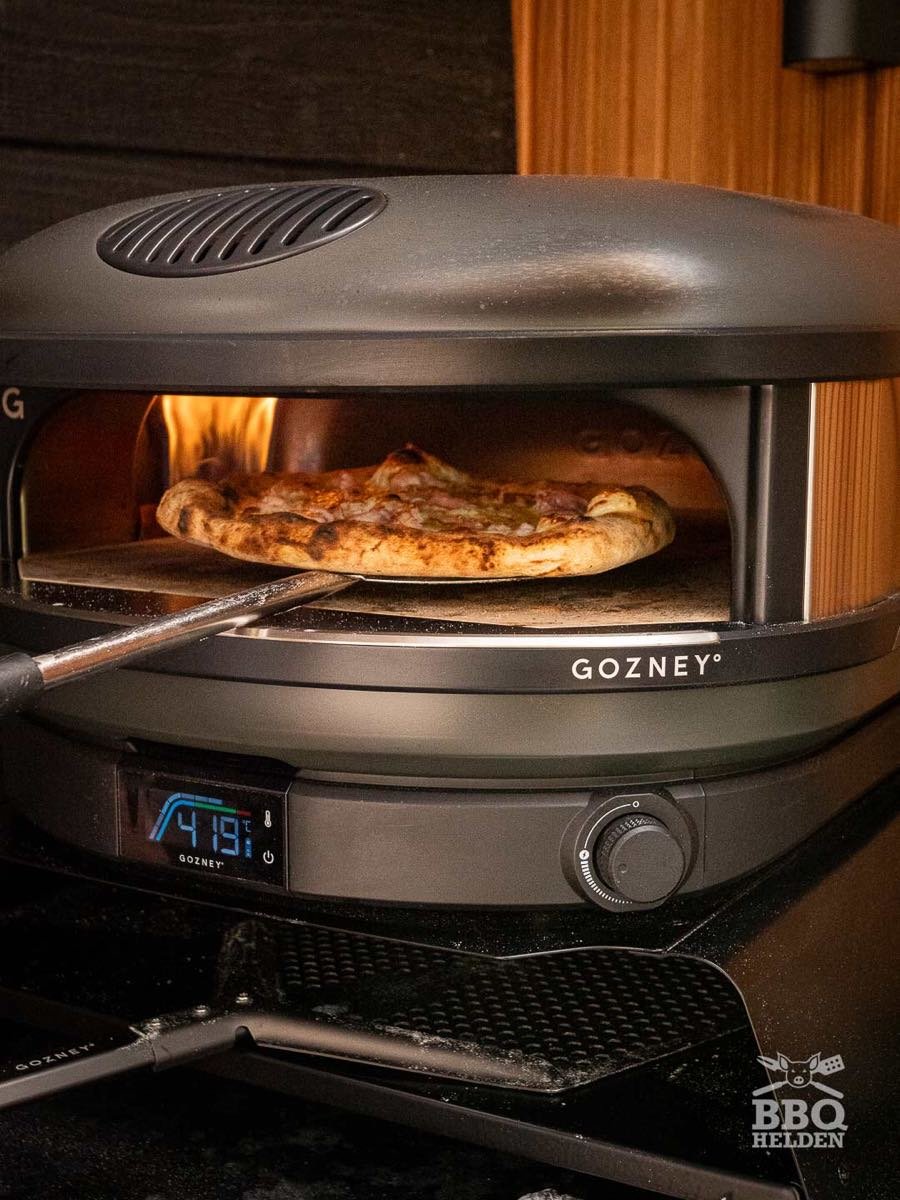 Frisch gebackene Pizza wird mit dem Schieber aus einem kuppelförmigen Pizza-Ofen gezogen, die Anzeige steht auf 419 Grad