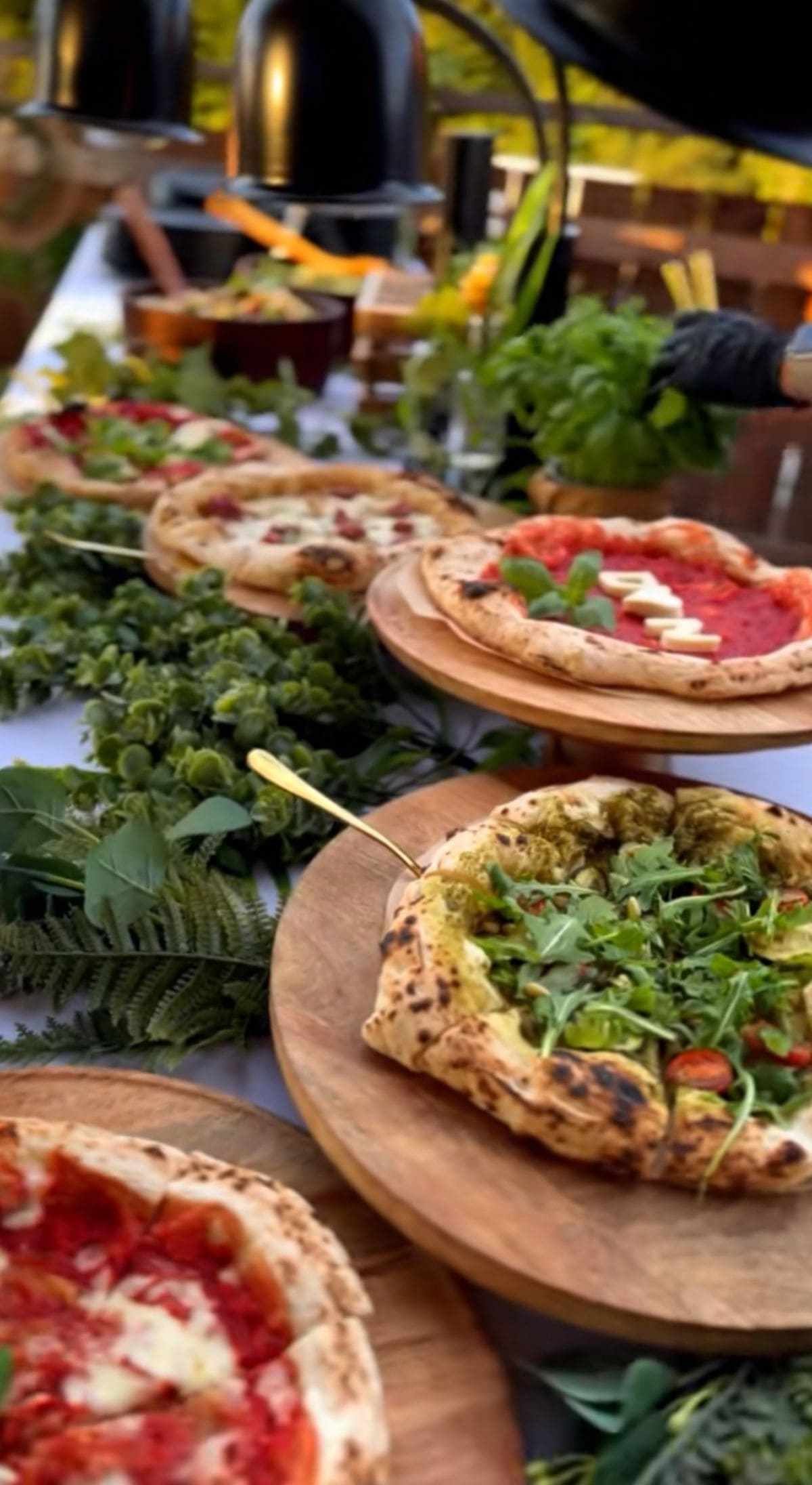 Frische Pizzen stehen auf Holzbrettern am Buffet bereit.